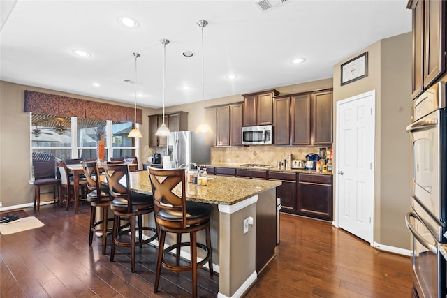 kitchen featuring a breakfast bar area, hanging light fixtures, stainless steel appliances, light stone counters, and an island with sink