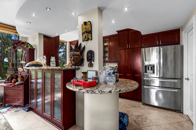 kitchen with stainless steel refrigerator with ice dispenser, kitchen peninsula, and stone counters