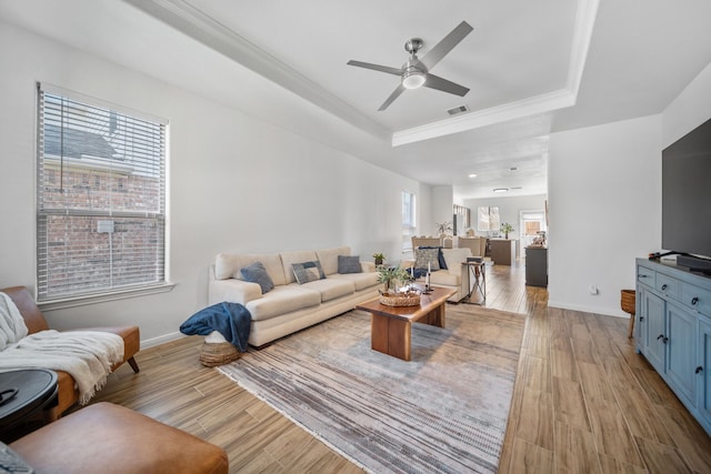 living room with ornamental molding, a raised ceiling, ceiling fan, and light wood-type flooring