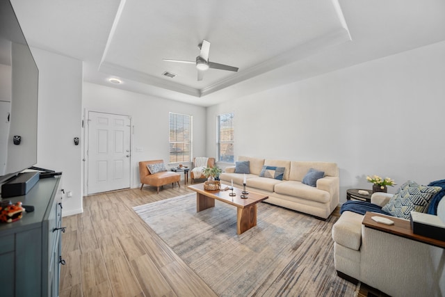 living room featuring a raised ceiling, ceiling fan, and light wood-type flooring