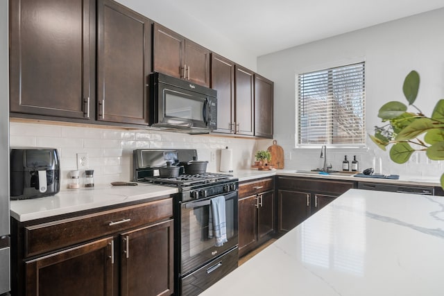 kitchen with sink, light stone counters, dark brown cabinets, decorative backsplash, and black appliances