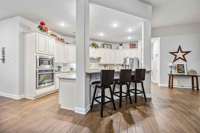 kitchen with white cabinetry, stainless steel appliances, dark hardwood / wood-style floors, light stone countertops, and a kitchen bar