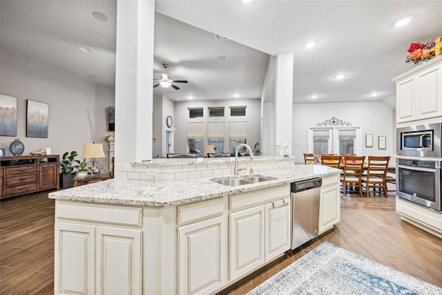 kitchen with sink, ceiling fan, appliances with stainless steel finishes, wood-type flooring, and light stone countertops