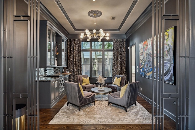 sitting room with ornamental molding, a tray ceiling, dark hardwood / wood-style flooring, and a notable chandelier