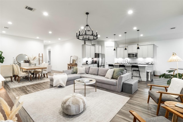 living room featuring an inviting chandelier, sink, and light hardwood / wood-style flooring