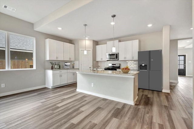 kitchen with appliances with stainless steel finishes, white cabinetry, hanging light fixtures, a kitchen island with sink, and light hardwood / wood-style floors