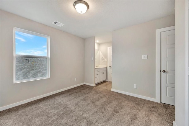 unfurnished bedroom with ensuite bathroom and light colored carpet