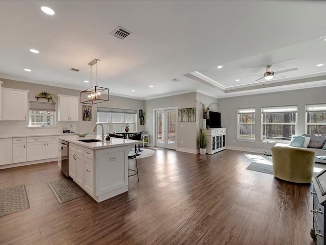 kitchen with sink, a kitchen island with sink, a kitchen breakfast bar, white cabinets, and stainless steel dishwasher