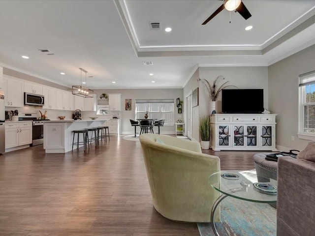 living room featuring hardwood / wood-style flooring, ornamental molding, a raised ceiling, and ceiling fan