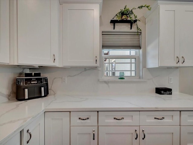 kitchen with tasteful backsplash, white cabinets, and light stone counters