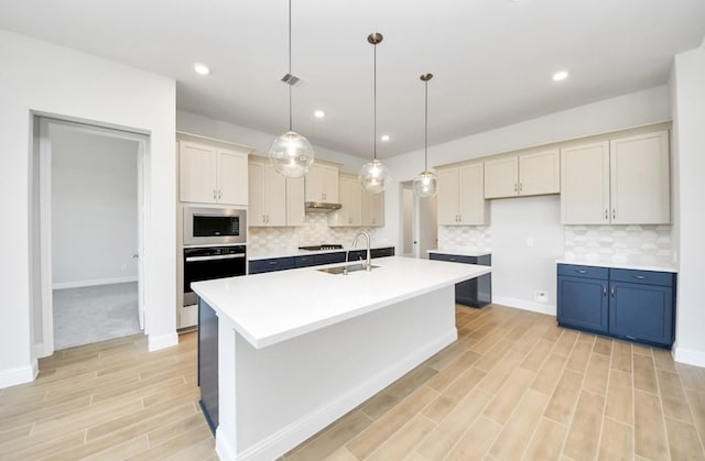 kitchen featuring decorative light fixtures, sink, decorative backsplash, stainless steel appliances, and a center island with sink