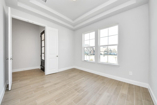 spare room featuring visible vents, a tray ceiling, light wood-style flooring, and baseboards