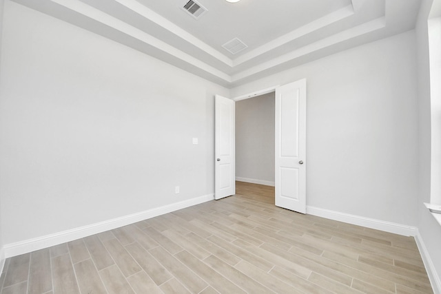 spare room featuring light wood-style flooring, visible vents, a raised ceiling, and baseboards