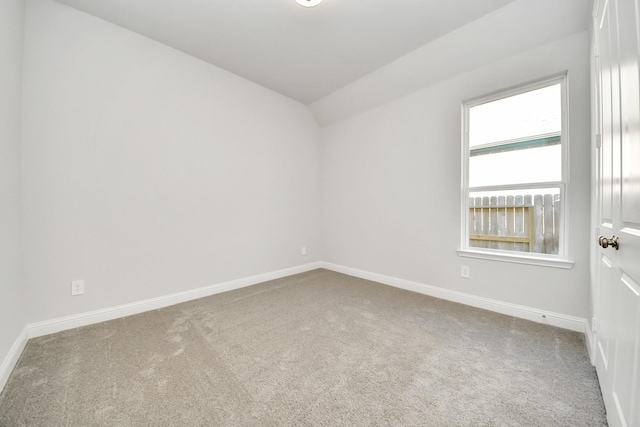 carpeted spare room with baseboards and vaulted ceiling