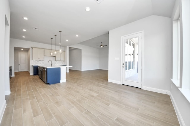 kitchen featuring light wood finished floors, decorative backsplash, a ceiling fan, open floor plan, and light countertops