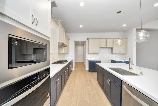 kitchen with appliances with stainless steel finishes, light countertops, a sink, and decorative light fixtures