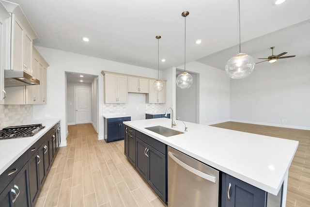 kitchen with under cabinet range hood, a sink, light countertops, appliances with stainless steel finishes, and light wood finished floors