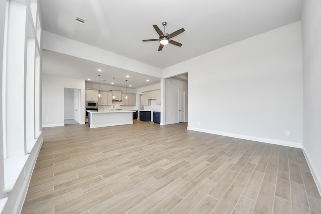 unfurnished living room with a ceiling fan, baseboards, visible vents, and light wood finished floors