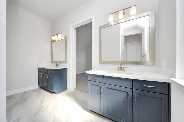 bathroom featuring marble finish floor, two vanities, a sink, and baseboards