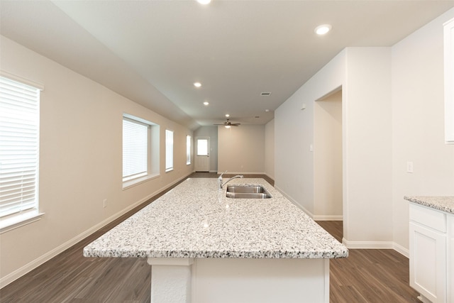 kitchen with dark hardwood / wood-style floors, an island with sink, sink, white cabinets, and light stone counters