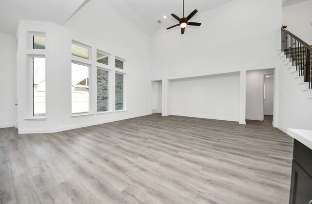 unfurnished living room featuring ceiling fan, stairway, a towering ceiling, and light wood-style floors