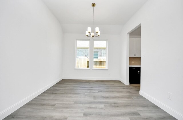 unfurnished dining area with light wood-style flooring, baseboards, and a notable chandelier