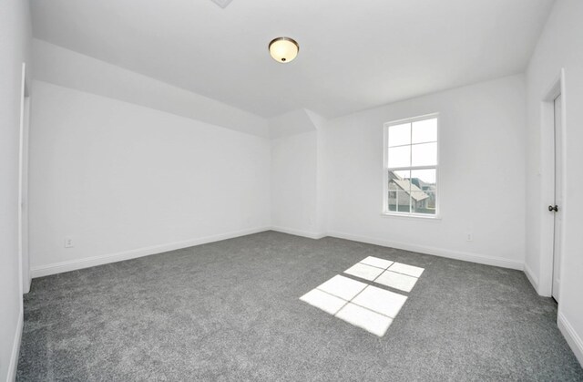 spare room with baseboards and dark colored carpet