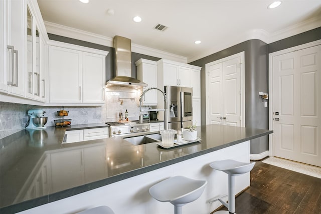 kitchen with dark countertops, stainless steel fridge, crown molding, and wall chimney range hood