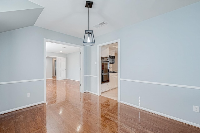 unfurnished dining area featuring vaulted ceiling and light hardwood / wood-style flooring