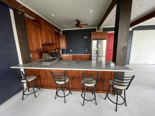 kitchen featuring stainless steel fridge, kitchen peninsula, ceiling fan, and a breakfast bar