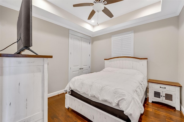 bedroom with dark hardwood / wood-style floors, a tray ceiling, ceiling fan, and a closet