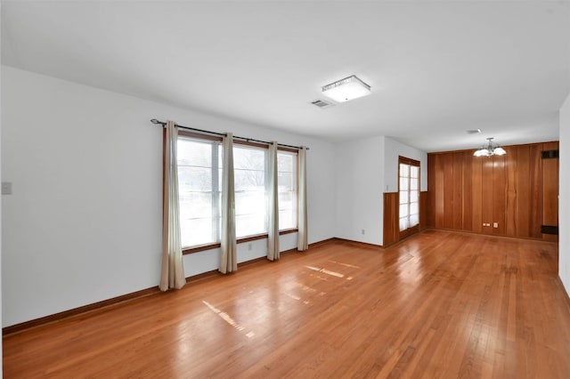 unfurnished living room with wooden walls, light hardwood / wood-style floors, and a chandelier