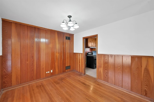 unfurnished room featuring an inviting chandelier, light hardwood / wood-style flooring, and wooden walls