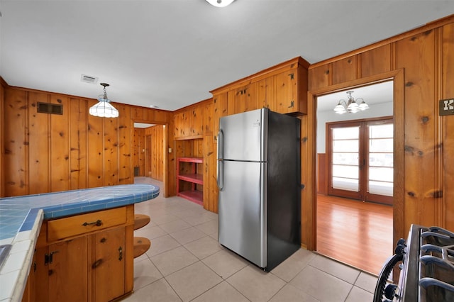 kitchen with wooden walls, stainless steel refrigerator, decorative light fixtures, stove, and tile counters