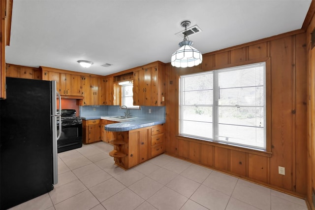 kitchen featuring sink, decorative light fixtures, stainless steel refrigerator, kitchen peninsula, and black gas range