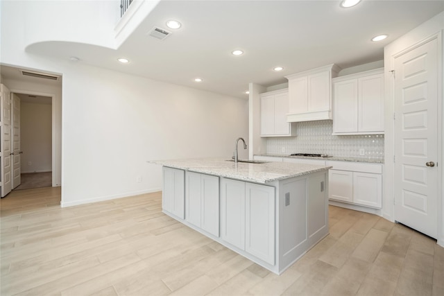 kitchen featuring a kitchen island with sink, sink, and white cabinets