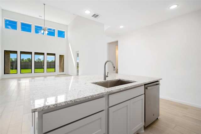 kitchen featuring sink, dishwasher, hanging light fixtures, light stone countertops, and an island with sink