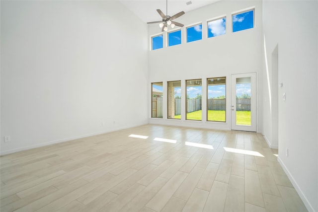 unfurnished living room with a towering ceiling, light hardwood / wood-style floors, and ceiling fan