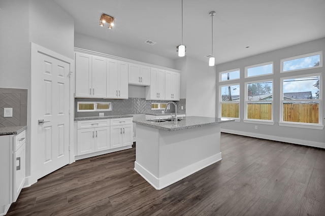 kitchen with white cabinetry, a kitchen island with sink, sink, and backsplash