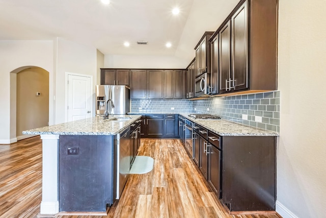 kitchen featuring sink, light hardwood / wood-style flooring, appliances with stainless steel finishes, light stone countertops, and a kitchen island with sink