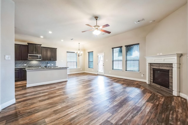 unfurnished living room featuring sink, ceiling fan with notable chandelier, a fireplace, and dark hardwood / wood-style flooring