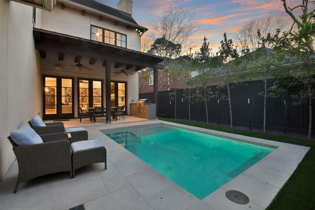 pool at dusk featuring a patio, ceiling fan, and exterior kitchen