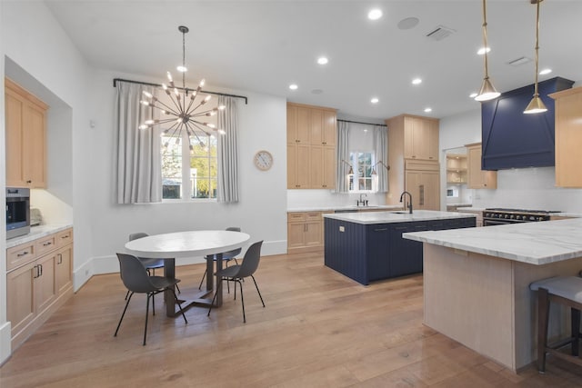 kitchen featuring a center island with sink, light brown cabinets, and decorative light fixtures