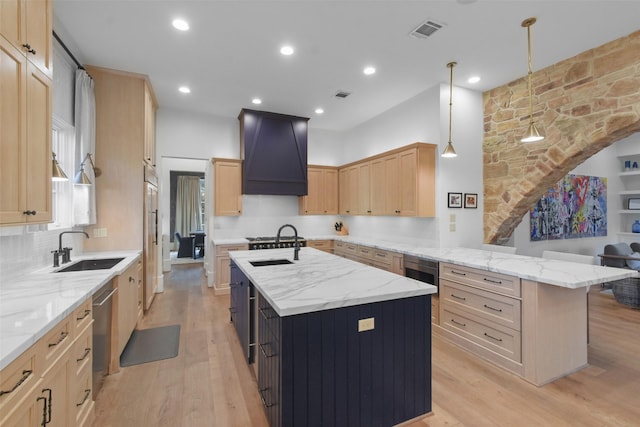 kitchen with an island with sink, custom exhaust hood, and light brown cabinets