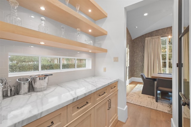 bar with light stone counters, lofted ceiling, light brown cabinetry, and light wood-type flooring