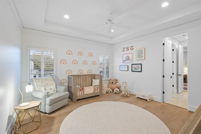 bedroom with ceiling fan, a raised ceiling, light hardwood / wood-style flooring, and a crib