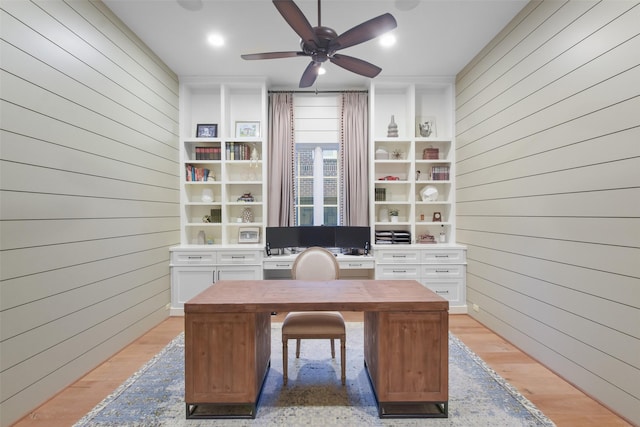 unfurnished office with ceiling fan, wooden walls, and light wood-type flooring