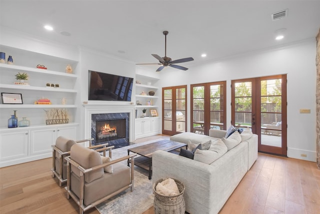 living room featuring light hardwood / wood-style flooring, a high end fireplace, built in features, and french doors