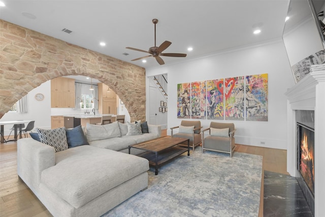 living room with sink, crown molding, hardwood / wood-style flooring, a premium fireplace, and ceiling fan