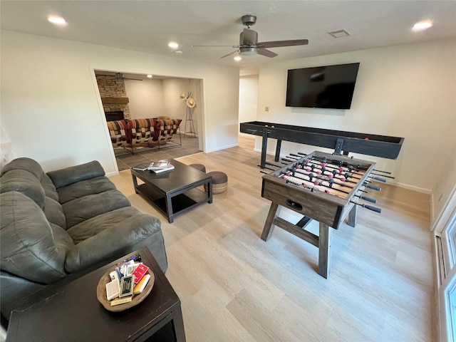 living room featuring ceiling fan, a stone fireplace, and light hardwood / wood-style floors